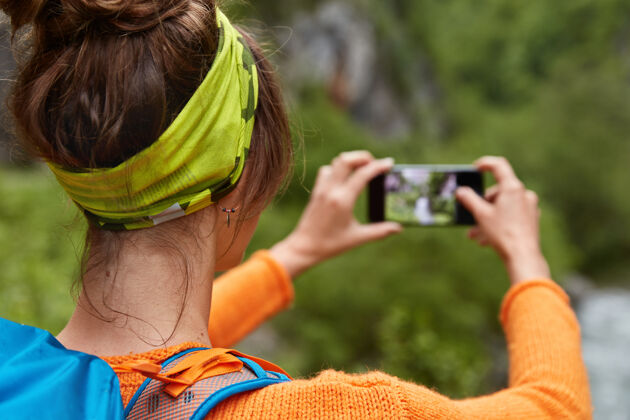 摄影师黑发女青年退后 戴着绿色头带 背着背包 在智能手机设备上拍照持有自然单独