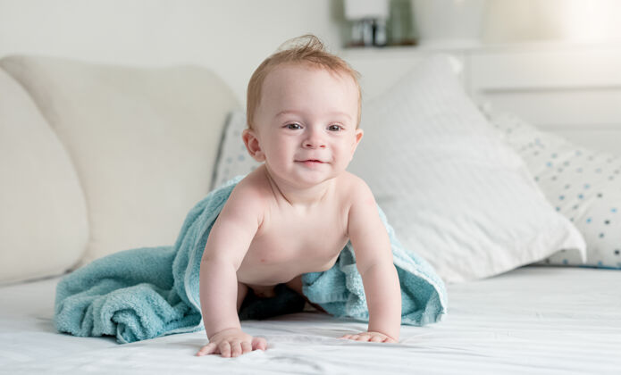 毯子美丽的9个月大的婴儿沐浴后在蓝色毛巾上爬在床上儿子玩谎言