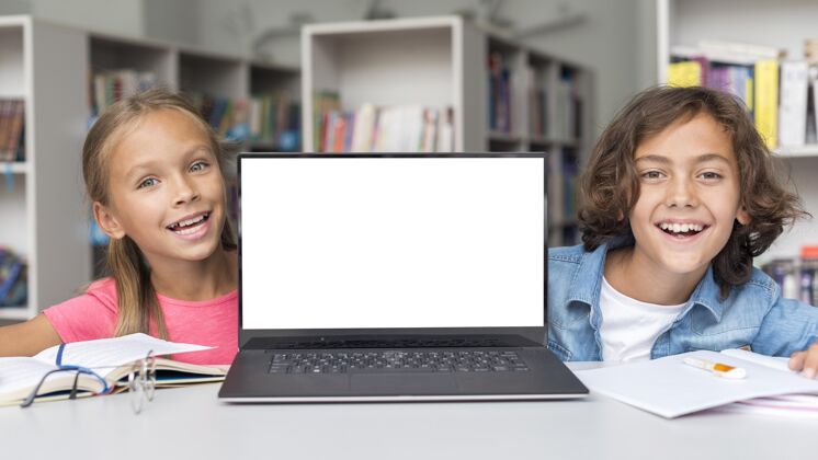小玩意男孩和女孩在图书馆与模拟笔记本电脑阅读学习设备