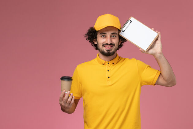 制服正面图：身穿黄色制服 披风的男性快递员手持咖啡杯和粉色墙上的记事本粉色杯子正面
