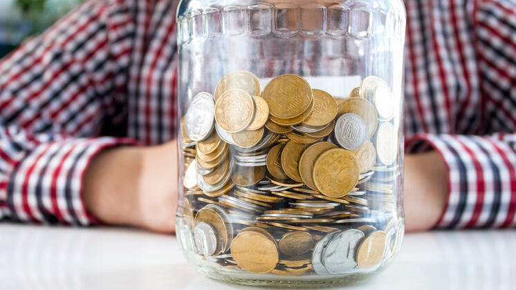 硬币坐在玻璃罐里装满硬币的人金融 经济增长和银行储蓄的概念给予现金工资