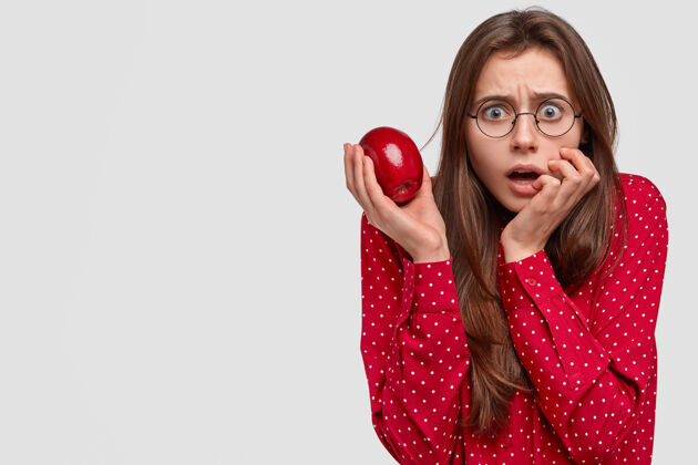 震惊惊艳动情的女士直视着恐惧的表情 手里拿着新鲜的红苹果女士素食饮食