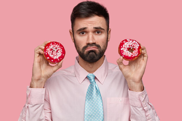 剃胡子照片中 一个满脸胡须的白种人愁眉苦脸 手里拿着两个甜甜圈 身着正装不高兴领带悲惨