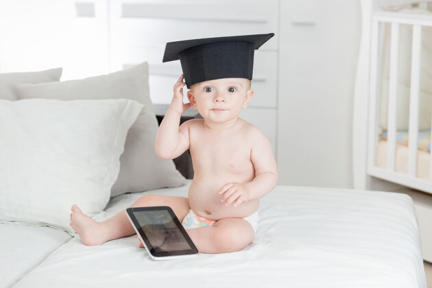 学校在毕业帽有趣的男婴肖像使用数字平板电脑天才技术人