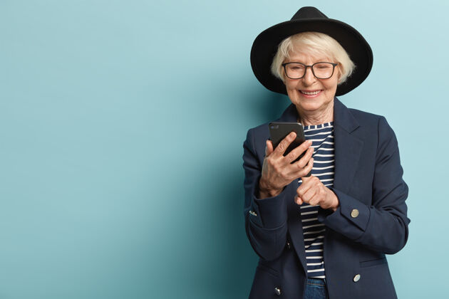 老年人高兴的老太太在智能手机上收到好消息 打字反馈 戴着时髦的黑帽子老年皱纹退休